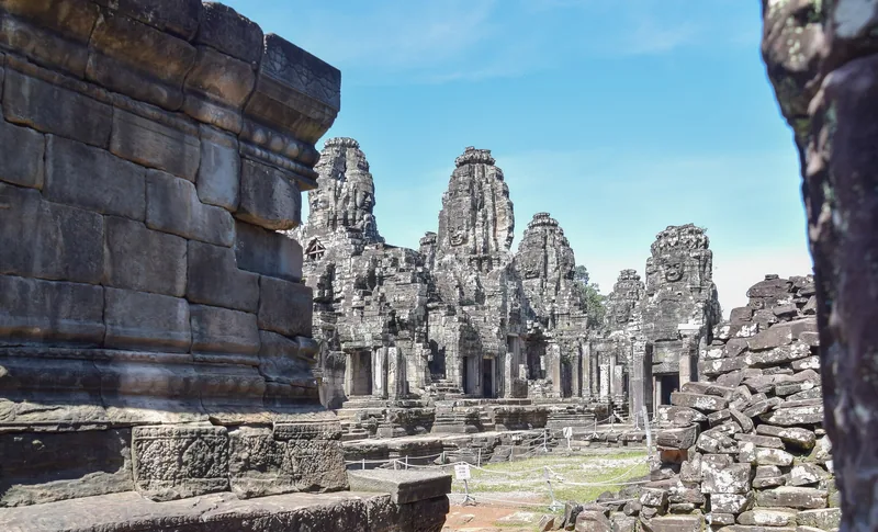 Stone face towers of Bayon Temple rise above ancient ruins under a clear blue sky in Siem Reap.
