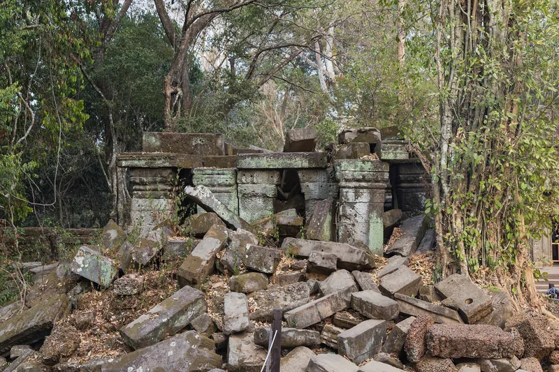 Collapsed sandstone blocks lie scattered among jungle trees at a ruined temple structure near Angkor, Siem Reap.