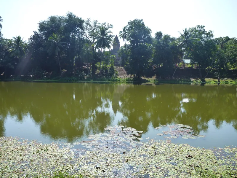 A pond with lily pads reflects palm trees and the tower of Prasat Bakong temple in Siem Reap.
