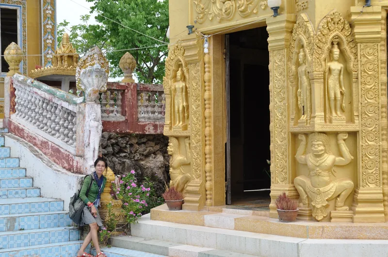 A visitor rests on tiled steps beside a golden ornate Khmer shrine entrance in Battambang, Cambodia.