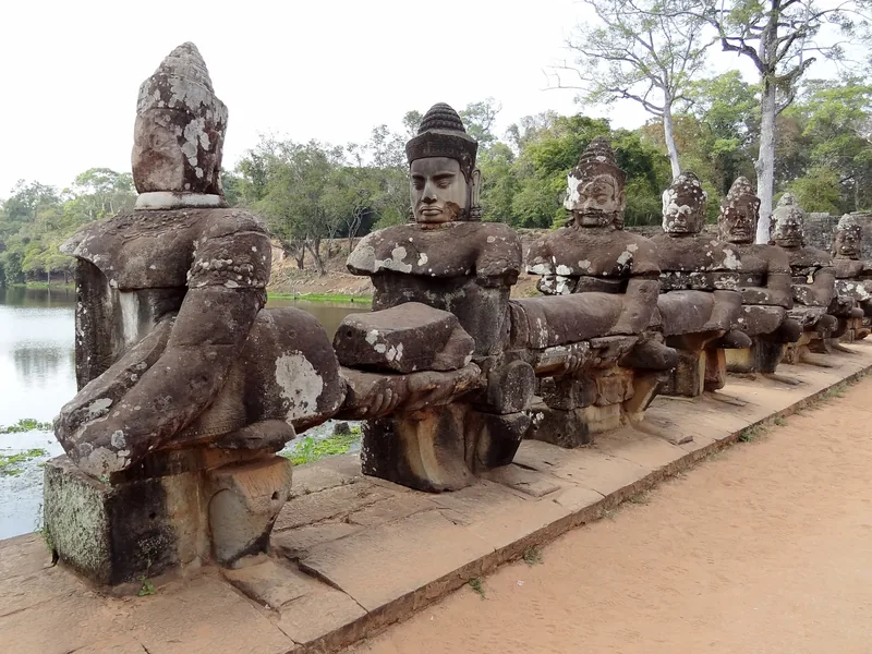 A row of weathered stone deity statues holding a naga balustrade along the causeway at Angkor Thom, Siem Reap.
