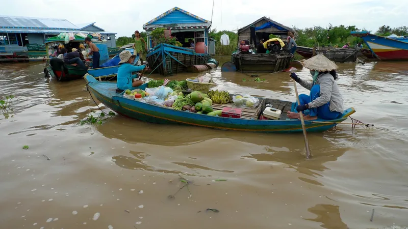 A vendor rows a boat loaded with fruits and vegetables past floating houses on Tonle Sap Lake near Siem Reap.