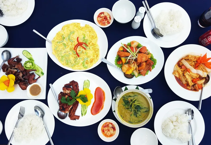 Overhead view of a Khmer meal in Siem Reap with omelette, grilled meat, soup and rice on a dark table