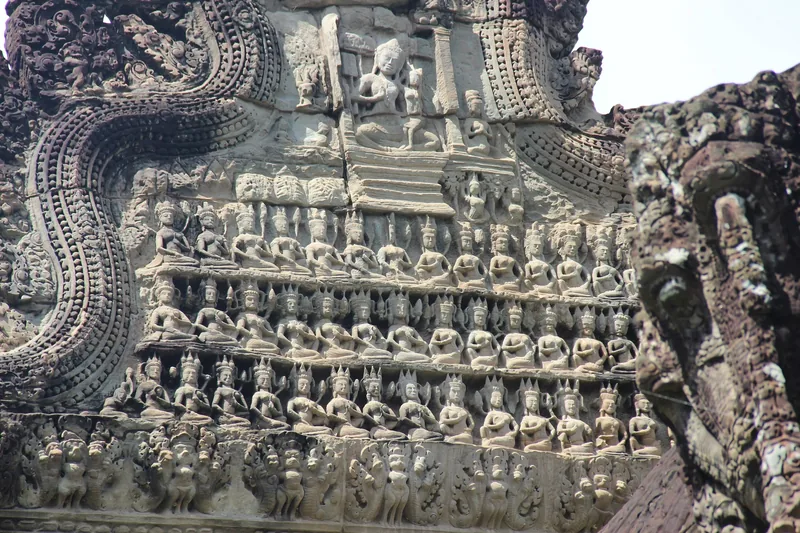 Intricate stone carvings of seated deities and naga motifs decorate a temple wall at Angkor Wat in Siem Reap.