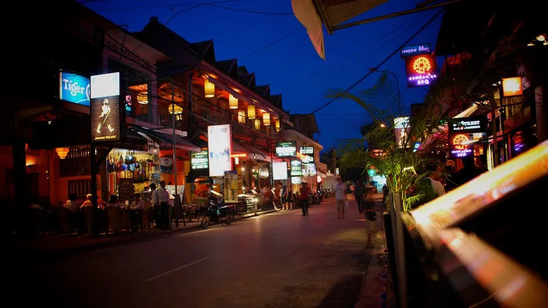 Neon signs and bar lights glow along a bustling street at dusk in Siem Reap.