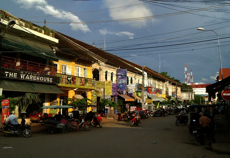 Colonial-era shophouses lined with signs and parked tuk-tuks along a street in Siem Reap.