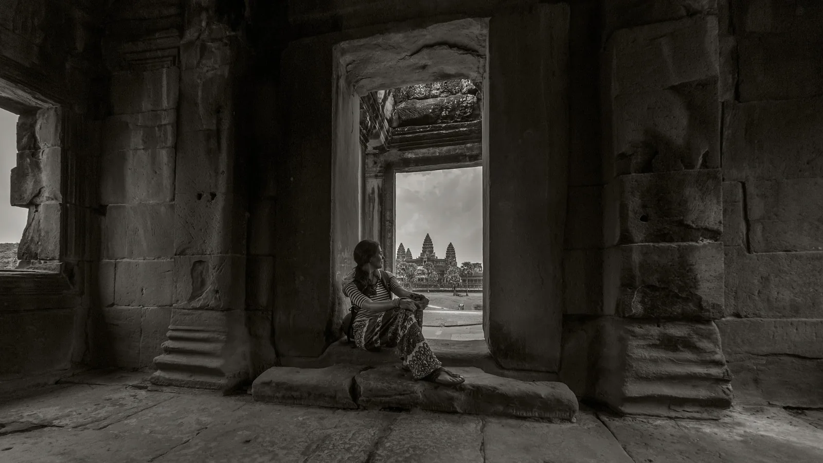 A woman sits in a stone window frame overlooking the towers of Angkor Wat near Siem Reap in this black-and-white photo.