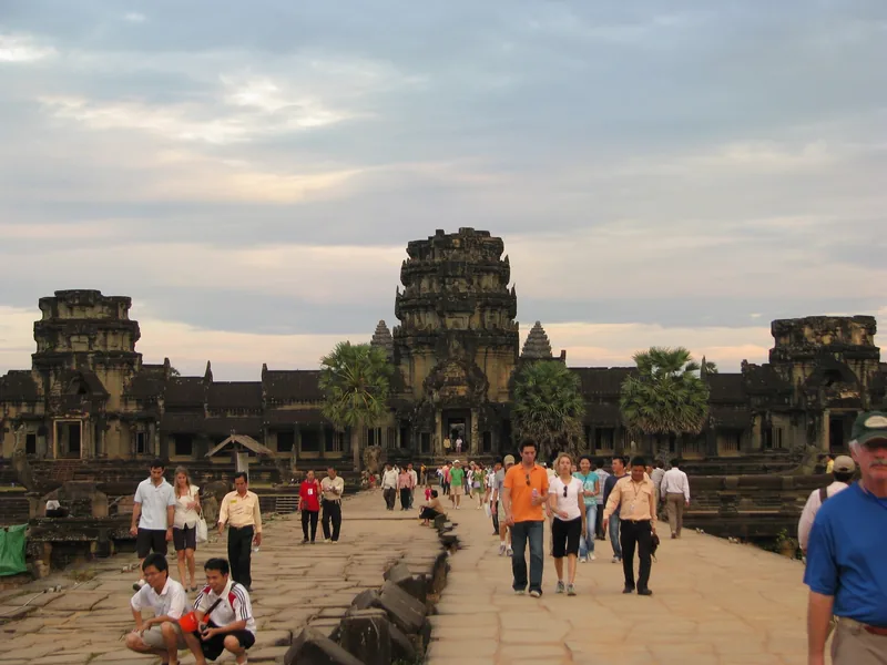 Tourists walk along the stone causeway toward the towers of Angkor Wat at dusk in Siem Reap.
