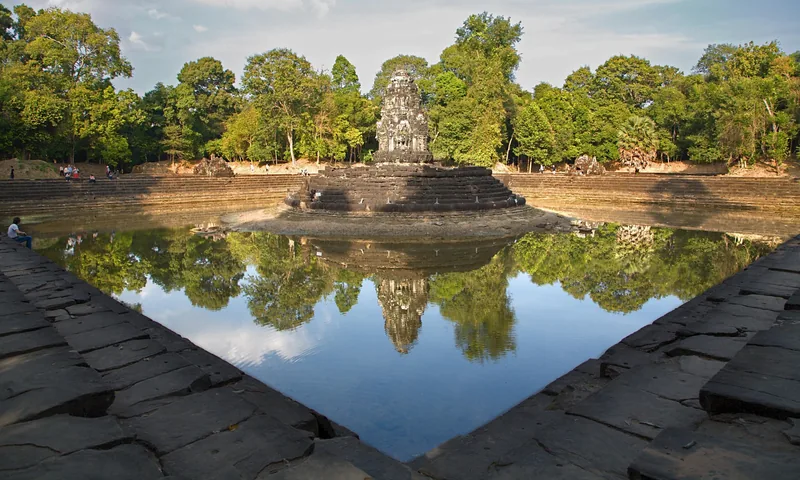 A stone temple tower rises from a circular island reflected in the still square pool of Neak Pean near Siem Reap.