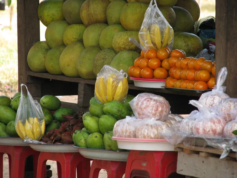A roadside stall in Siem Reap displays pomelos, oranges, mangoes, and peeled fruit on stacked red stools.