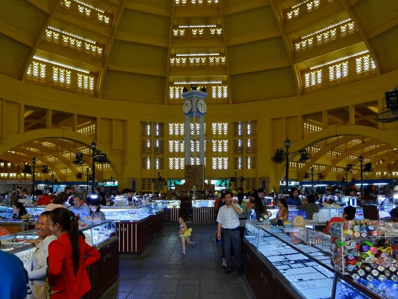 The domed central hall of Phnom Penh's Central Market with jewelry stalls and shoppers under a central clock tower.