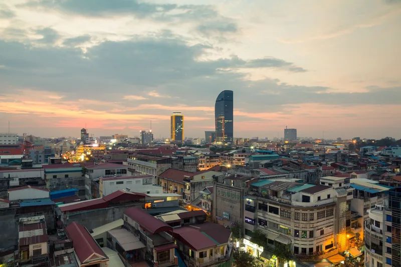 Sunset over Phnom Penh's skyline with modern towers rising above rooftops of low-rise buildings.