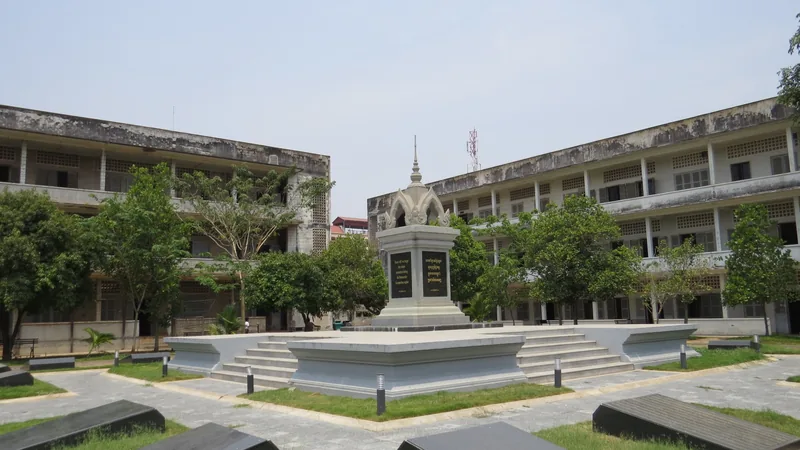 A memorial monument stands in the courtyard of Tuol Sleng Genocide Museum surrounded by weathered classroom buildings in.