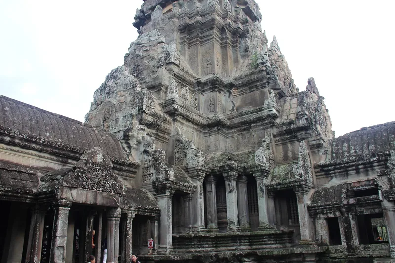 The towering central sanctuary of Angkor Wat rises above weathered stone galleries under a pale sky.