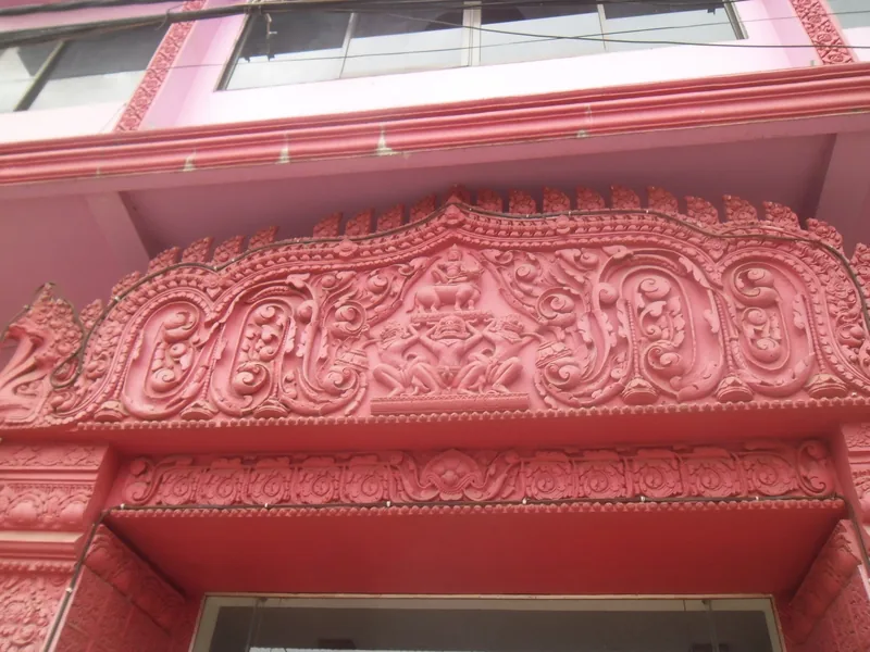 Ornate carved pediment with scrollwork decorates a pink building entrance in Siem Reap, Cambodia.
