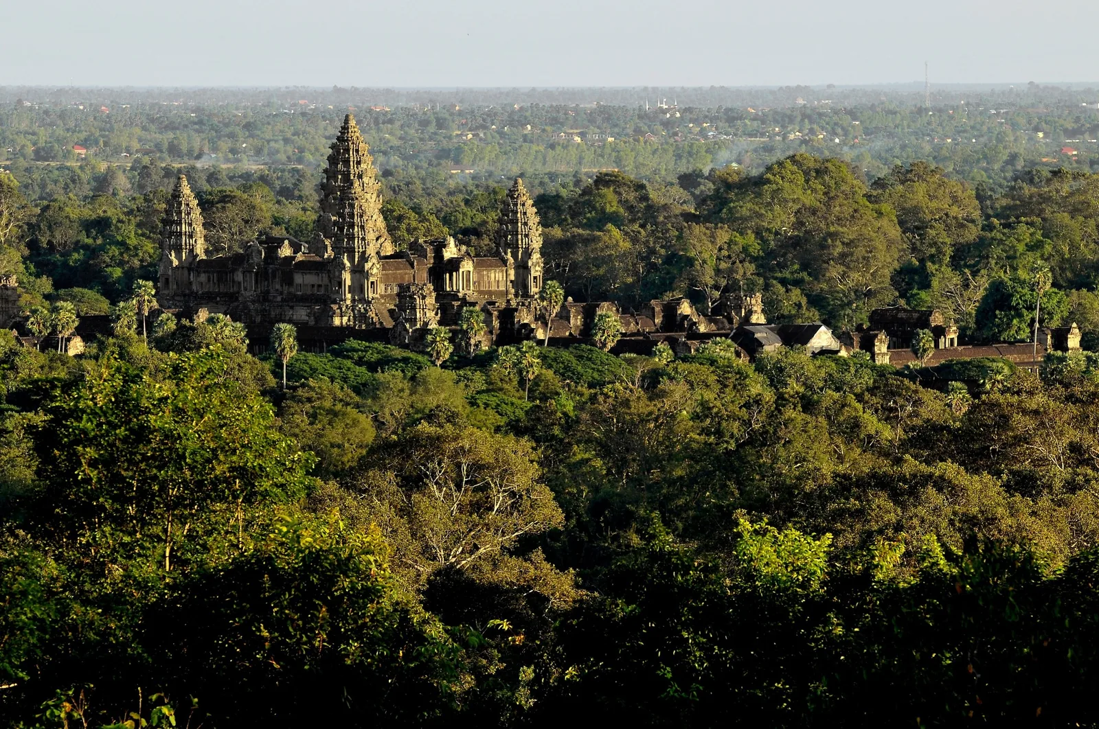 The towering spires of Angkor Wat rise above a dense green forest canopy near Siem Reap. The towering spires of Angkor Wat rise above a dense green forest canopy near Siem Reap.