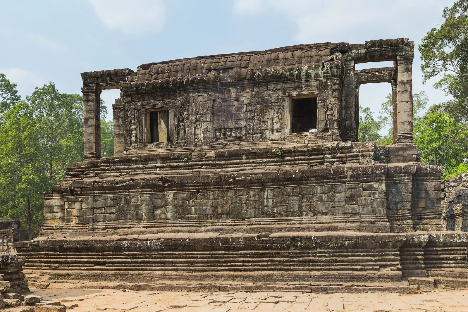 Ancient stone temple ruins with carved reliefs stand beside trees at Angkor Thom near Siem Reap. Ancient stone temple ruins with carved reliefs stand beside trees at Angkor Thom near Siem Reap.